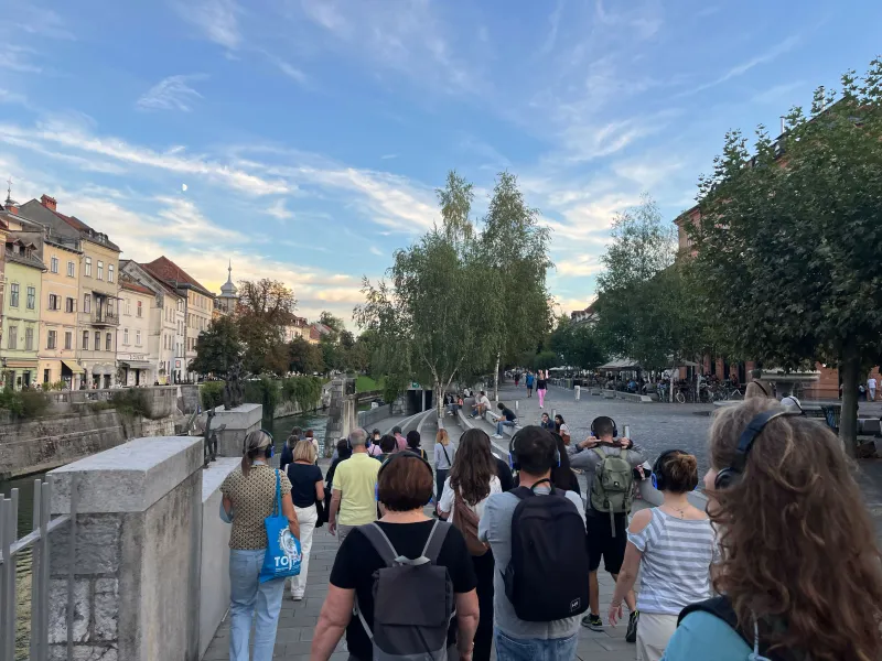 Ljudje s slušalkami med sprehodom po Ljubljani, ob bregu Ljubljanice.